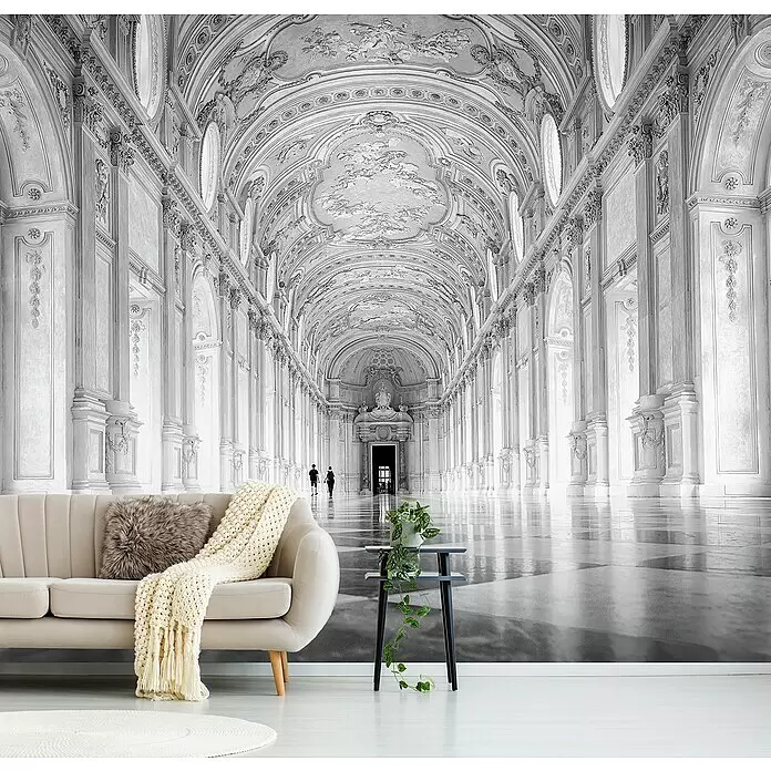 Papermoon Premium collection Fototapete Im Licht verloren - B x H: 500 x 280 cm, Vlies - Ein beiges Sofa mit einer cremefarbenen Decke und Pflanze auf einem Tisch in einem Raum mit einem großen, grauen architektonischen Gangwandbild.
