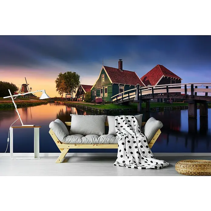 Papermoon Premium collection Fototapete Haus an der Zaan - B x H: 300 x 223 cm, Vlies - Das Bild zeigt ein modernes Sofa mit Kissen und einer gepunkteten Decke vor einer malerischen Landschaft.