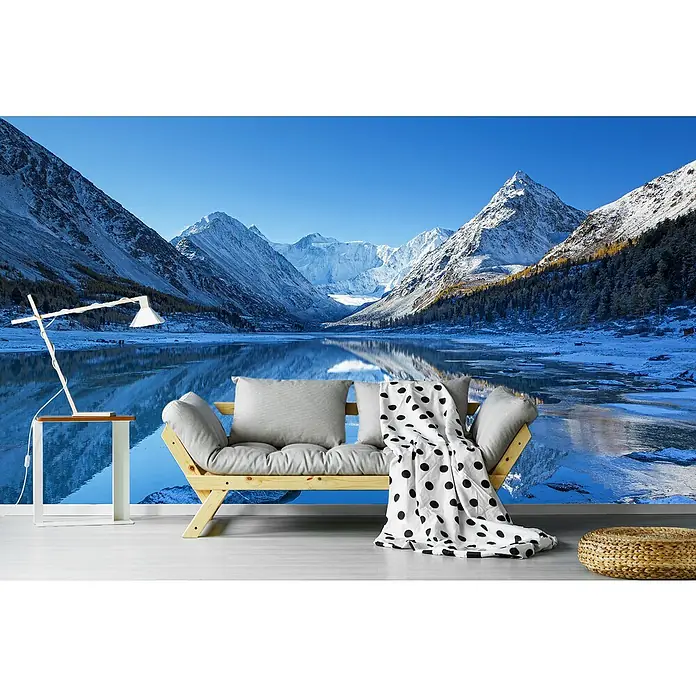 Papermoon Premium collection Fototapete Akkem See - B x H: 500 x 280 cm, Vlies - Das Bild zeigt ein stilvolles Zimmer mit Blick auf eine atemberaubende Berglandschaft. Im Vordergrund steht ein bequemes Sofa mit Kissen und Decke.