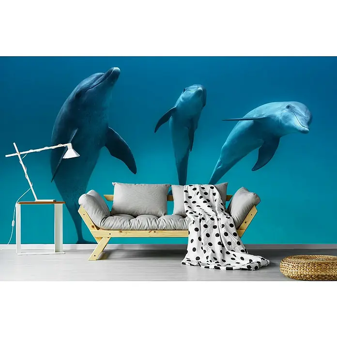 Papermoon Premium collection Fototapete Tümmler - B x H: 500 x 280 cm, Vlies - Ein Zimmer mit einer Holzcouch, einem Beistelltisch mit Lampe und einer Wandtapete mit Delfinen, die ein ruhiges maritimes Flair erzeugen.