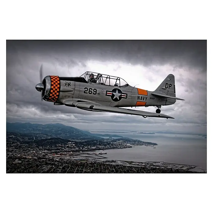 Papermoon Premium collection Fototapete Über unter - B x H: 350 x 260 cm, Vlies - Nahaufnahme eines grauen Marineflugzeugs, das über eine Küstenstadt fliegt, mit sich drehendem Propeller und klarer Kennzeichnung.