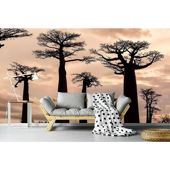 Papermoon Premium collection Fototapete Madagaskar - B x H: 500 x 280 cm, Vlies - Wohnzimmer mit Designlampe, Futonbett und einem Hocker. Im Hintergrund eine Fototapete mit Bäumen bei Sonnenuntergang.