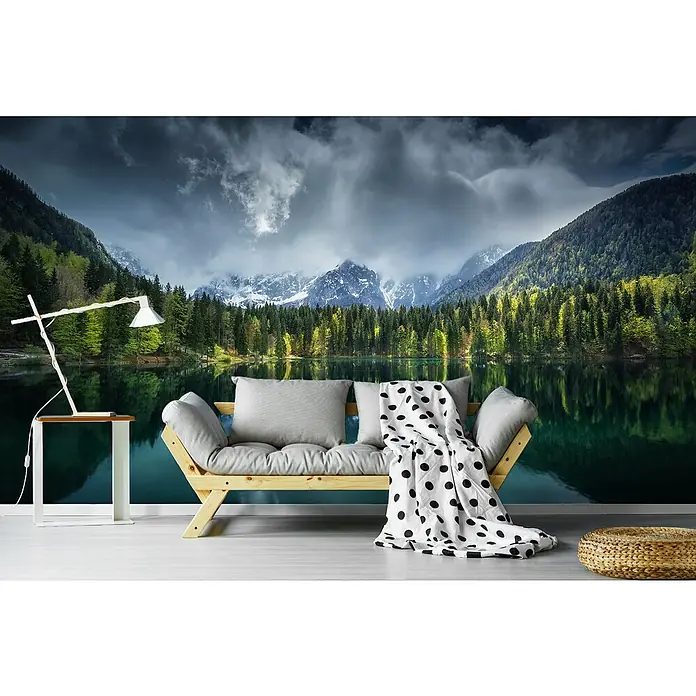 Papermoon Premium collection Fototapete Bergsee bewölkter Tag - B x H: 300 x 223 cm, Vlies - Ein gemütliches Zimmer mit einer Couch, einer Lampe und einem Hocker vor einer Tapete mit Bergmotiven.