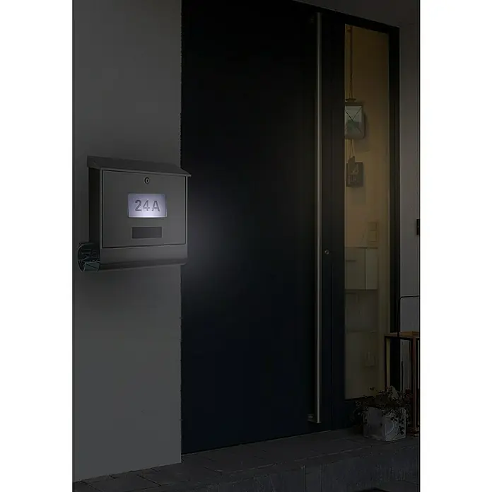 Portaferm Wandbriefkasten Solar - L x B x H: 12 x 38,5 x 41 cm, Silber, Edelstahl, Zeitungsfach - Eine moderne Briefkastenanlage mit beleuchteter Hausnummer 24A neben einer Haustür in dunkler Umgebung.