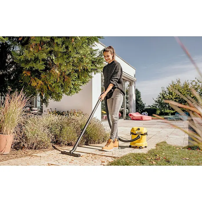 Kärcher Elektro-Nass- & Trockensauger WD 2 PLUS V-12/4/18 - 1.000 W, Behältervolumen: 12 l - Eine Frau, die einen gelben Kärcher Mehrzwecksauger zum Reinigen der Terrasse verwendet, während sie im Freien steht.