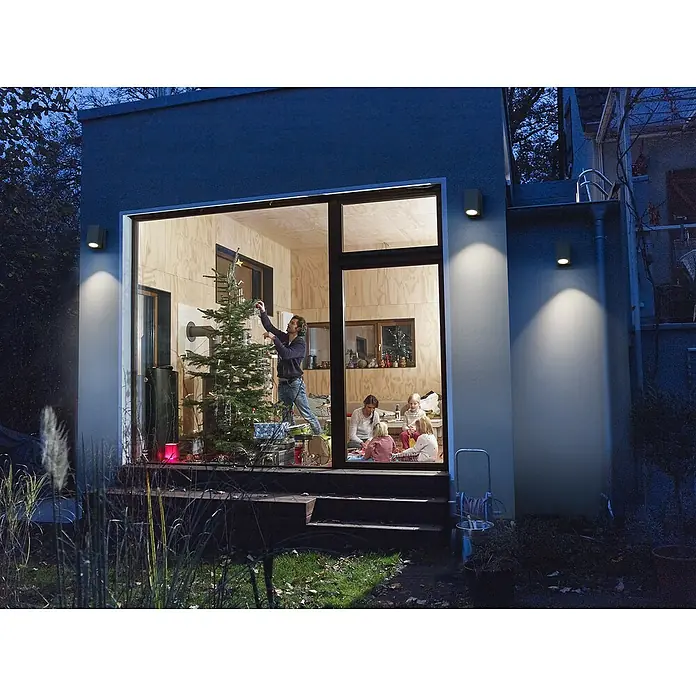 Ledvance Außenwandleuchte Endura Cube - 35 W, 6,6 x 9,3 x 10 cm, Schwarz, IP44 - Beleuchtete Außenwandleuchten erhellen ein modernes Haus mit einer Familie, die drinnen einen Weihnachtsbaum schmückt, und sorgen für eine warme Atmosphäre.