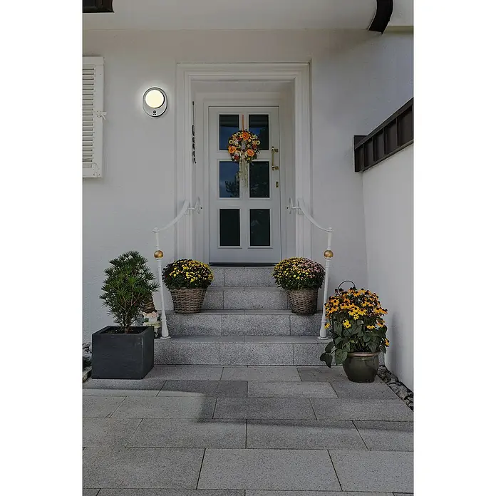 Osram LED-Außenwandleuchte Endura Disc Wall - 8 W, 24,4 x 20 x 6 cm, Silber, IP44 - Eine einladende Haustür mit einem runden, modernen LED-Außenleuchte an der Seite, umgeben von saisonaler Dekoration.