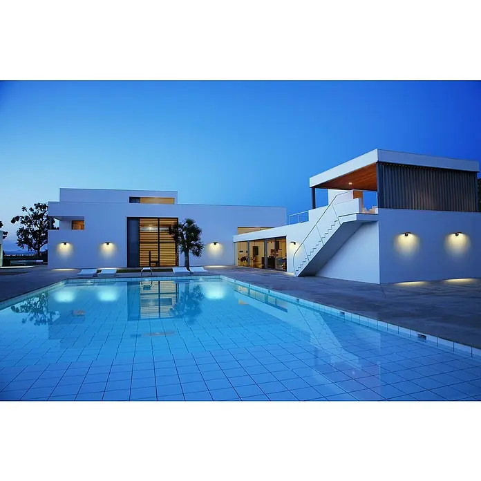 Ledvance Solar-Außenwandleuchte Endura Style Solar - 3,6 W, L x B x H: 16 x 17,7 x 8 cm, Dunkelgrau, IP44, 180 lm - Moderne Villa mit Pool bei Dämmerung. Das Haus besticht durch klare Linien, weiße Fassade und elegante Außenbeleuchtung, die eine stimmungsvolle Atmosphäre schafft.