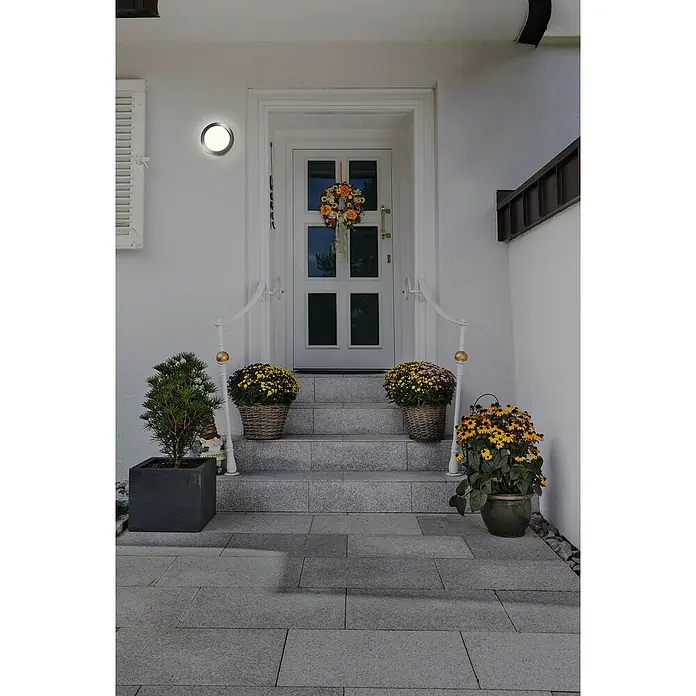 Osram LED-Außenwandleuchte Endura Disc Wall - 8 W, 20 x 20 x 6 cm, Silber, IP44 - Eingangsbereich eines Hauses mit Blumen geschmückt. Die Haustür ist mit einem Herbstkranz dekoriert, während die Treppen mit Blumenarrangements verziert sind.
