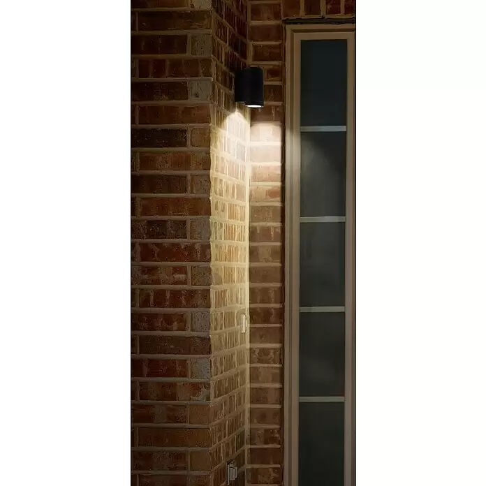 Osram Endura Classic Außenwandleuchte Beam - 35 W, 10,4 x 9,2 x 14,6 cm, Dunkelgrau, IP44 - Schwarze zylindrische Außenwandleuchte an einer Ziegelwand, die warmes Licht nach oben und unten wirft.