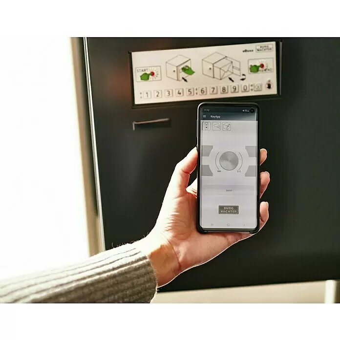 Burg-Wächter Paketbox eBoxx GV 645 - L x B x H: 45 x 57,5 x 76 cm, Anthrazit, Stahl, Namensschild, Fassungsvermögen: 197 l - Hand hält Smartphone mit 'KeyApp' zur Steuerung eines Smart-Schließsystems, gezeigt mit einer Anweisungstafel.