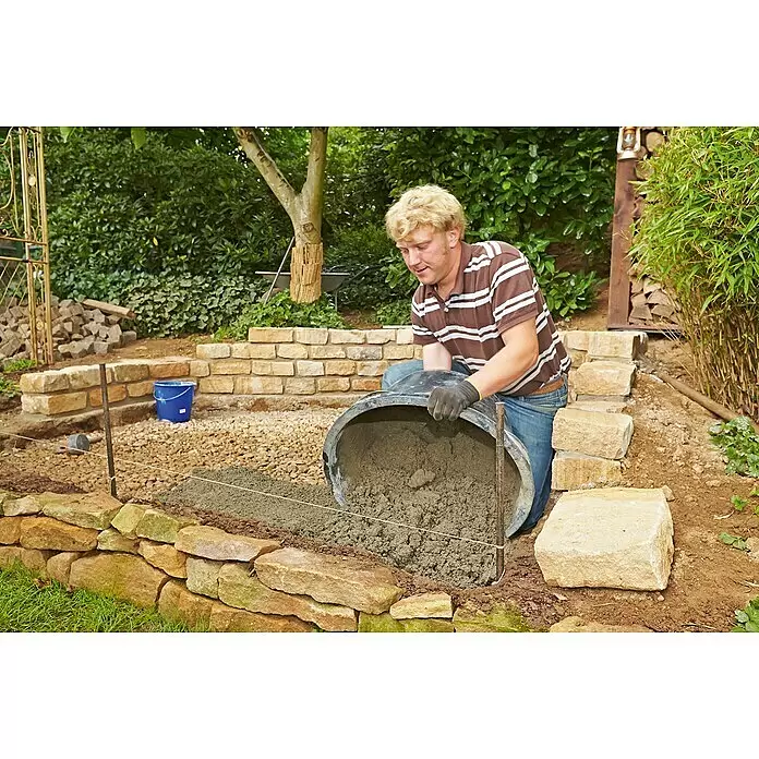 Quick-Mix Drainagemörtel - 25 kg - Mann schüttet grauen Beton aus schwarzem Eimer zum Legen eines Fundaments für eine Steinmauer.