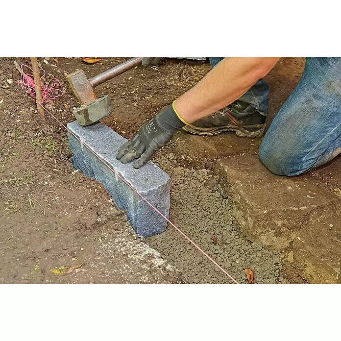 Quick-Mix Gartenbaubeton mit Trass - 30 kg - Dunkelgrauer Granitbordstein wird als Randstein verlegt, mit einer Richtschnur ausgerichtet und mit einem Hammer eingesetzt.