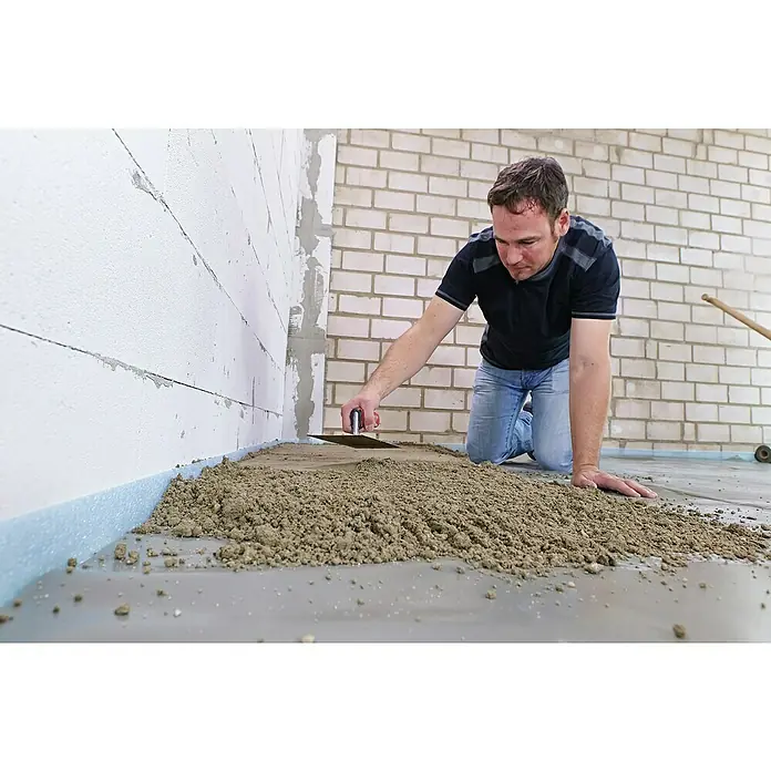 Quick-Mix Estrichbeton B03 - 40 kg - Ein Mann kniet und verteilt Estrichmasse mit einer Kelle auf einem Untergrund, um einen ebenen Boden zu schaffen.