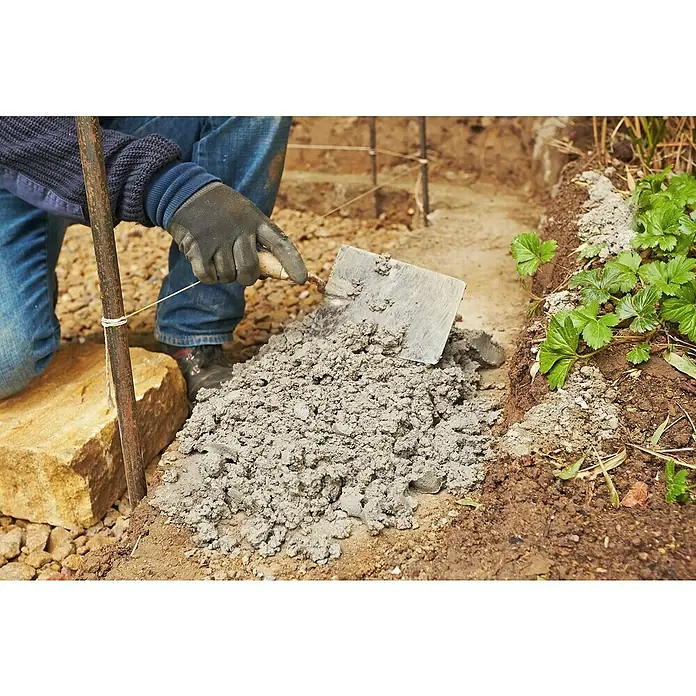 Quick-Mix Gartenmauermörtel - 30 kg - Ein Arbeiter glättet mit einer Kelle Beton für einen Gartenweg. Die Kelle und der graue Beton stehen im Fokus des Bildes.