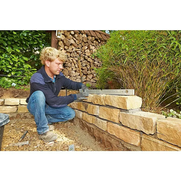 Quick-Mix Gartenmauermörtel - 30 kg - Der Bau einer rustikalen Steinmauer mit einem erfahrenen Handwerker, der präzise eine Wasserwaage verwendet.
