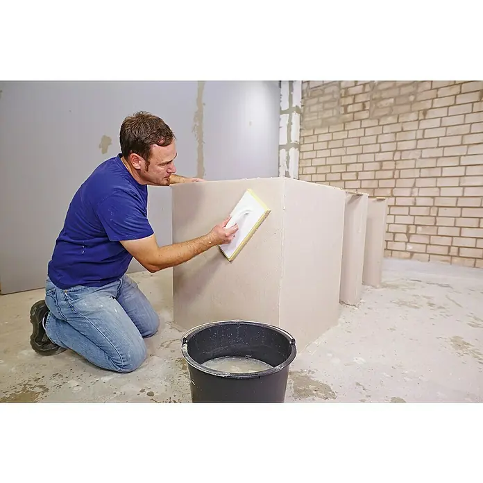 Quick-Mix Hagalith Kalkzement-Haftputz FF - 40 kg - Handwerker beim Verputzen eines Mauerwerks mit einem Putzwerkzeug in einem Rohbau. Der Eimer steht daneben.