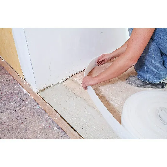 Quick-Mix Ausgleichsmasse Sicher+Plan XXL - 20 kg, Schichtdicke: 2 mm - 60 mm - Trittschalldämmung wird an einer Wand angebracht. Die weiße Isolierung ist aufgerollt und bereit zur Verwendung für die Schallreduzierung.