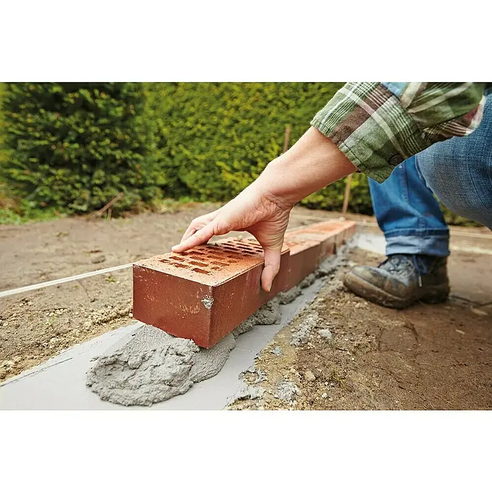 Quick-Mix Zementmörtel Z01 - 40 kg - Ein Maurer legt einen roten Ziegelstein auf eine Schicht Mörtel, um eine stabile und dauerhafte Konstruktion zu schaffen.