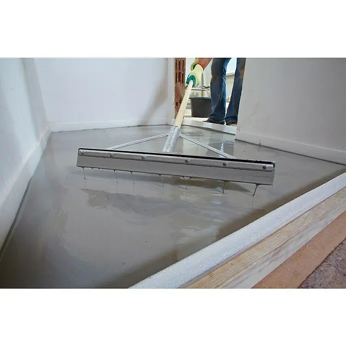 Quick-Mix Ausgleichsmasse Sicher+Plan XXL - 20 kg, Schichtdicke: 2 mm - 60 mm - Bildausschnitt einer Nivelliermasse, die mit einer Rakel auf einem Boden verteilt wird. Ein Arbeiter nivelliert den Untergrund, um ein ebenes Ergebnis zu erzielen.