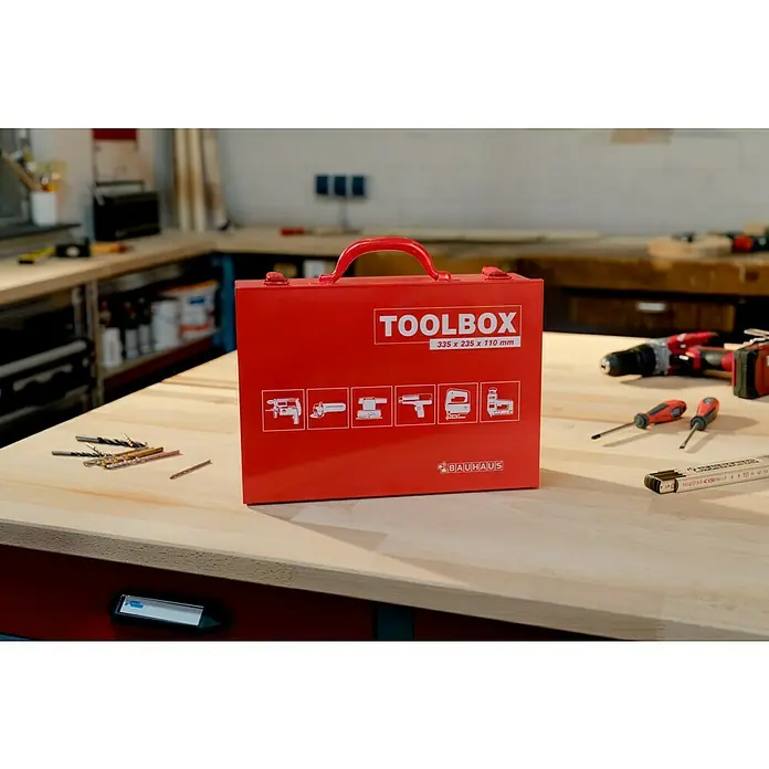 BAUHAUS Maschinenkoffer Toolbox - 33,5 x 23,5 x 11 cm, Geeignet für: Uni-Elektrowerkzeuge, Stahl - Ein roter Werkzeugkoffer von Bauhaus auf einer Werkbank, umgeben von Werkzeugen.