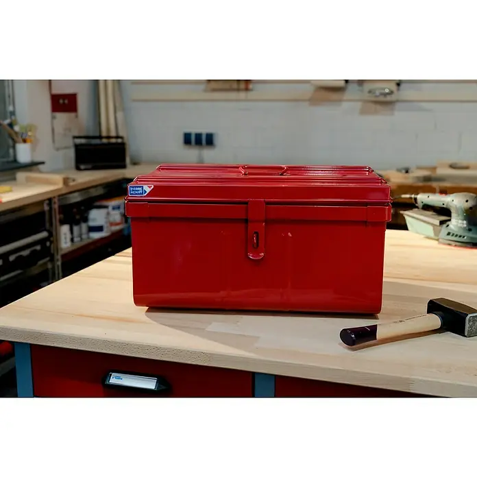 Aufbewahrungs- & Transportbox Motobox - 53 x 37 x 29 cm, Rot - Ein roter Pierre Henry Werkzeugkasten steht auf einer Werkbank, daneben ein Hammer, im Hintergrund ein Schleifgerät.