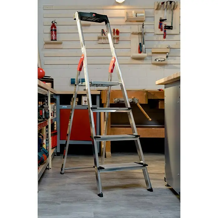 Hailo Stehleiter XXL - Anzahl Tritte: 4 Stk., Arbeitshöhe: 2,6 m, Belastbarkeit: 150 kg, Aluminium - Eine silberne Haushaltsleiter mit vier Stufen steht in einer Werkstatt mit Werkzeugen und Werkbänken. Praktisch für Arbeiten in der Höhe.