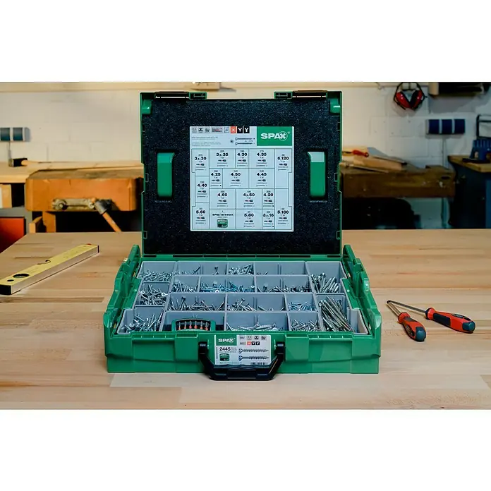 Spax Kit de tornillos L-Boxx - 2.447 pzs. - Una caja Spax bit box verde abierta llena de varios tornillos está sentada sobre una mesa de madera, herramientas cerca.