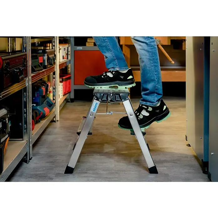 Krause Klapptritt Treppy - Anzahl Tritte: 4 Stk., Arbeitshöhe: 2,45 m, Belastbarkeit: 150 kg, Aluminium - Eine Person steht auf einer Krause-Trittleiter mit schwarzen Atlas-Sicherheitsschuhen, die auf einem grauen Boden steht.