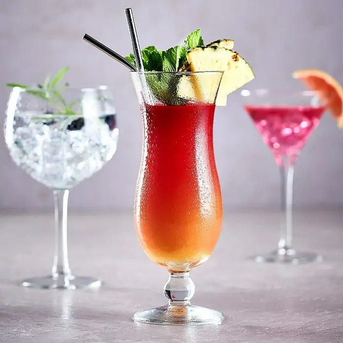 Set de copas de coctelería - Vidrio, 6 pzs. - Un cóctel refrescante adornado con piña, servido en un elegante vaso con pajitas, junto a otras bebidas coloridas.