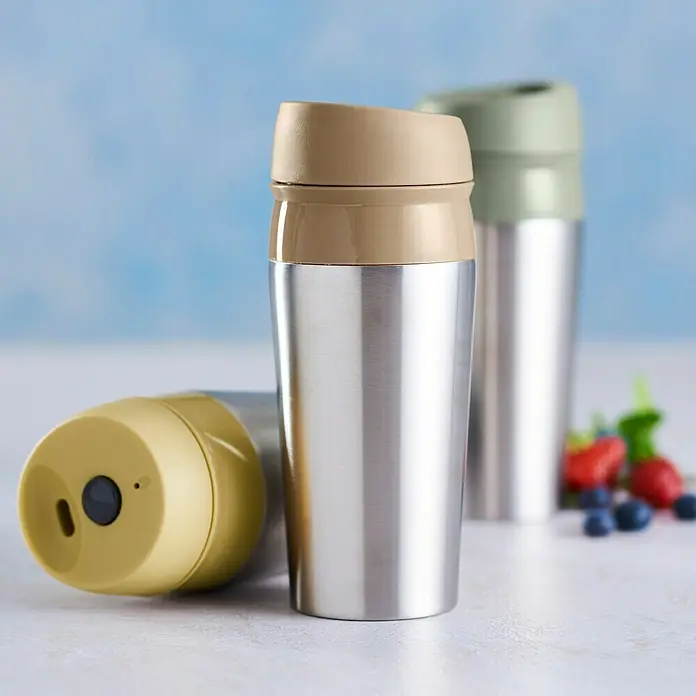 Termo para beber hermético - Ø x Al: 8 x 21 cm, 450 ml - Primer plano de tres vasos de acero inoxidable con tapas de colores sobre una mesa con fondo borroso.