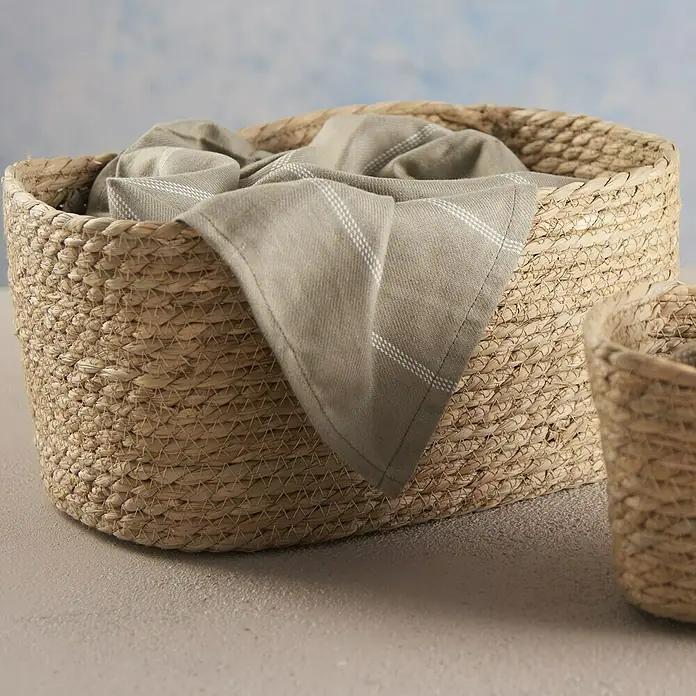 Cesta de junco - L x An x Al: 24 x 34 x 17 cm, Natural - Una cesta de paja con un paño gris dentro, ideal para guardar objetos o como elemento decorativo en el hogar.