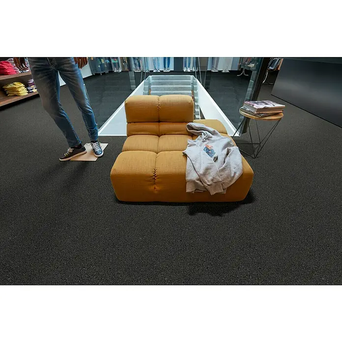 Beauflor PVC-Boden Meterware Titan - 400 cm, Scala, Schwarz/Grau - Die graue Kapuzenjacke mit Print auf einer gelben Couch bietet Komfort und Stil in einem modernen Geschäftsumfeld.