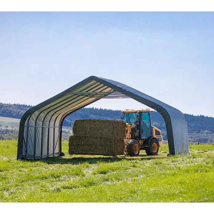 ShelterLogic Garage - 730 x 680 x 380 cm, Stahl - Eine landwirtschaftliche Szene mit einer Heuballenlagerhalle und einem Traktor, der Heuballen transportiert.