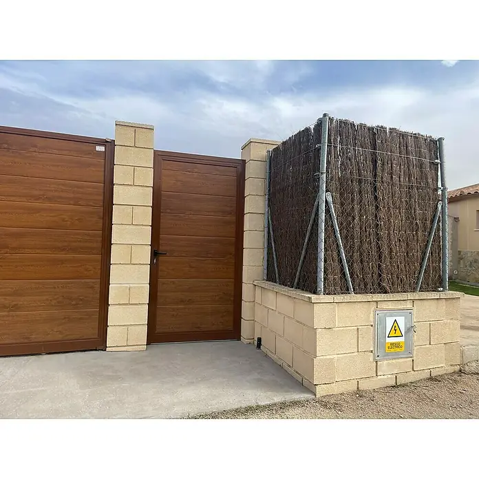 Brezo Eco 1 - 5 x 2 m, Marrón - Una puerta de madera marrón y una valla con una señal de advertencia amarilla "Risiko Electrico", que aseguran un acceso seguro a la propiedad.