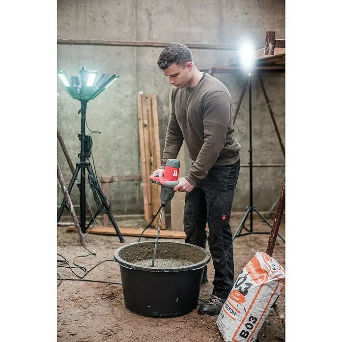 Berg Tecmix Handrührwerk TMX PRO 1600 - Durchmesser Rührer: 160 mm, Leistungsaufnahme: 1.600 W - Ein Bauarbeiter mischt Beton mit einem roten Handrührgerät in einem schwarzen Eimer, Betonmischer im Einsatz.