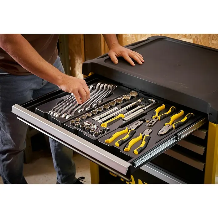 Stanley Carro portaherramientas STST74305-1 - L x An x Al: 67,6 x 42,6 x 85,9 cm, Número de cajones: 5 ud., Capacidad de carga: 300 kg - Un hombre mete la mano en una caja de herramientas llena de variedad de herramientas, incluyendo llaves inglesas, juego de vasos, carracas y alicates.