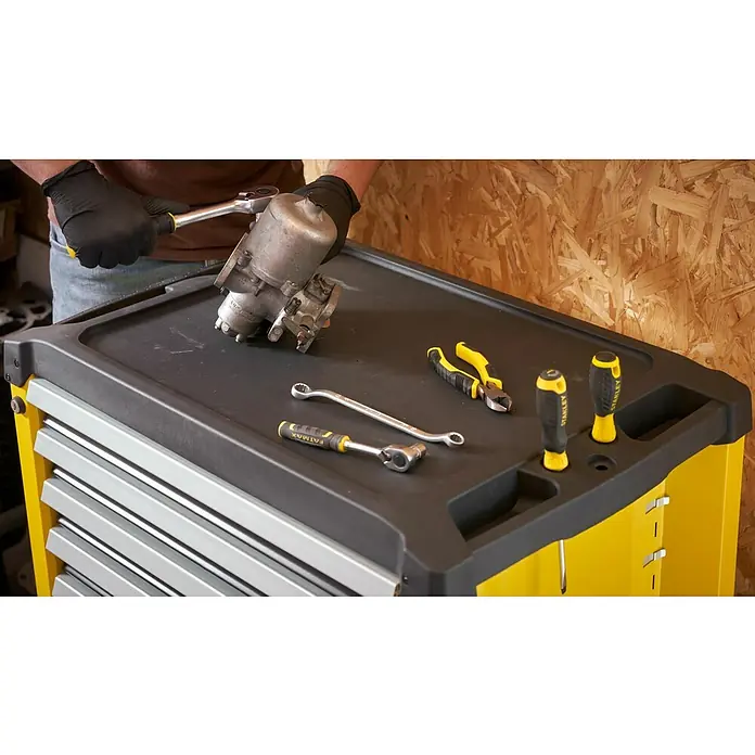 Stanley Carro portaherramientas STST74306-1 - L x An x Al: 74 x 45,9 x 89,8 cm, Número de cajones: 7 ud., Capacidad de carga: 300 kg - Un banco de trabajo con una variedad de herramientas, como llaves, alicates y destornilladores, ordenados sobre una superficie de trabajo negra.