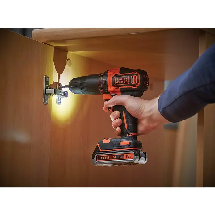 Black+Decker Taladro atornillador percutor de batería BDCHD18KB2 - 18 V, 2 baterías, 2 Ah, 40 Nm - Primer plano de un taladro atornillador inalámbrico Black+Decker que sujeta una bisagra a un armario de madera.