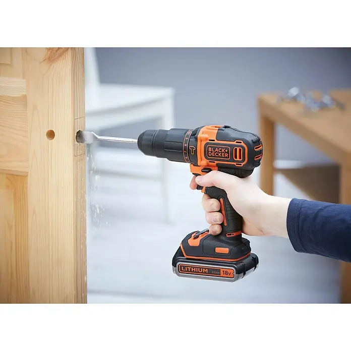 Black+Decker Taladro atornillador percutor de batería BDCHD18KB2 - 18 V, 2 baterías, 2 Ah, 40 Nm - Un taladro inalámbrico Black+Decker perforando un trozo de madera, con virutas de madera que salen volando del taladro.