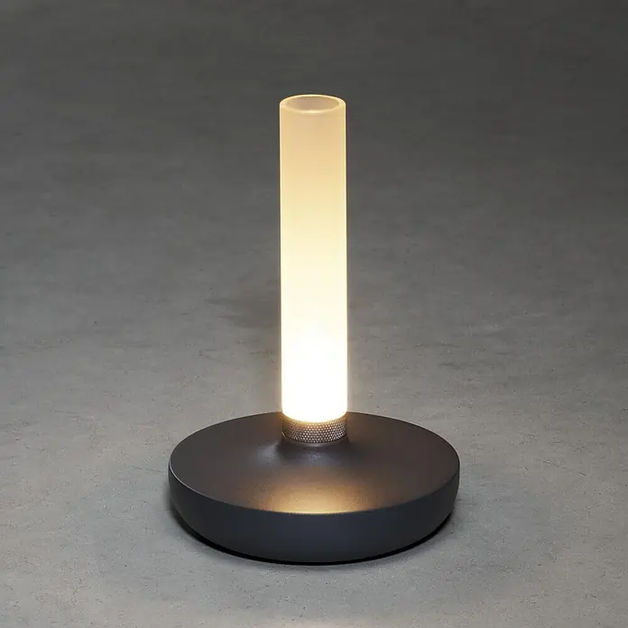 Konstsmide Akku-Tischleuchte Biarritz - 2,5 W, L x B x H: 13,5 x 13,5 x 20,5 cm, Grau, Warmweiß - Eine moderne Tischleuchte mit einem runden Sockel und einem leuchtenden, zylindrischen Lampenschirm, die ein warmes Licht verbreitet.