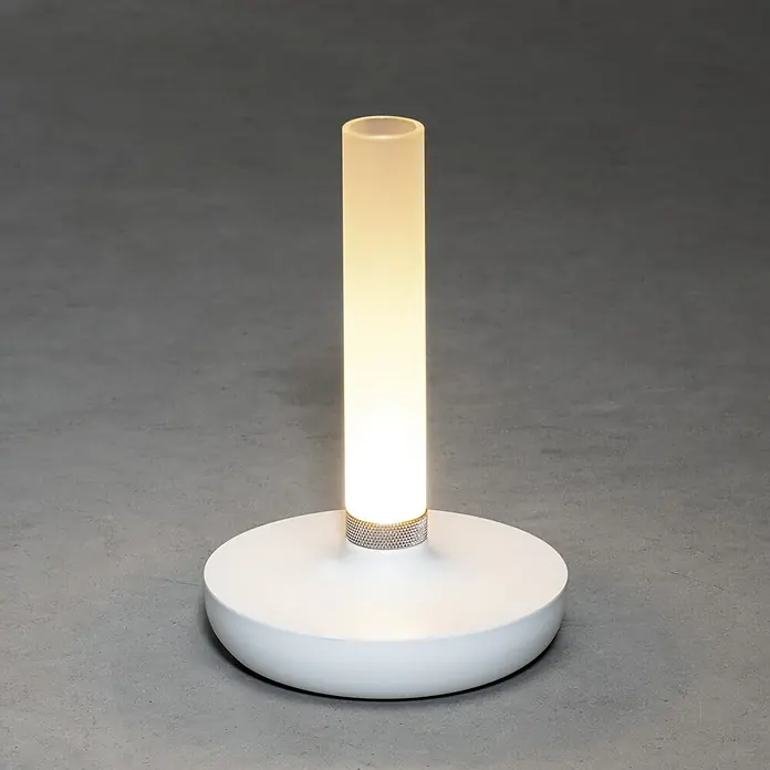 Konstsmide Akku-Tischleuchte Biarritz - 2,5 W, L x B x H: 13,5 x 13,5 x 20,5 cm, Weiß, Warmweiß - Nahaufnahme einer modernen Tischleuchte mit zylindrischem Lampenschirm und rundem Sockel, die ein warmes, gedämpftes Licht ausstrahlt.