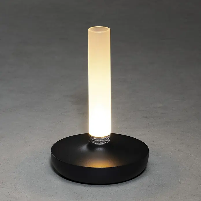 Konstsmide Akku-Tischleuchte Biarritz - 2,5 W, L x B x H: 13,5 x 13,5 x 20,5 cm, Schwarz, Warmweiß - Nahaufnahme einer modernen Tischleuchte mit schwarzem Sockel und zylindrischem, mattiertem Schirm, die ein warmes Licht ausstrahlt.