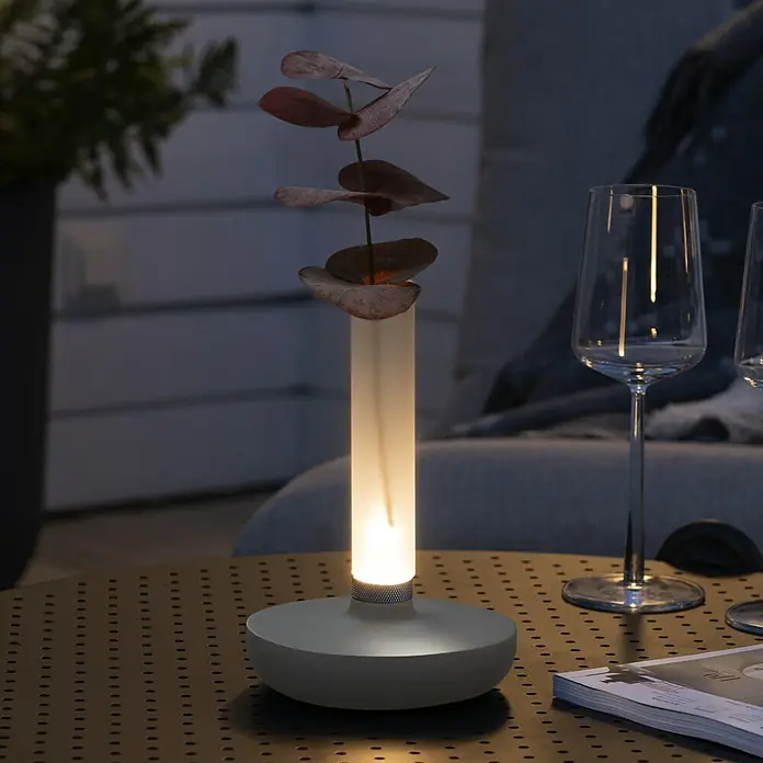 Konstsmide Akku-Tischleuchte Biarritz - 2,5 W, L x B x H: 13,5 x 13,5 x 20,5 cm, Weiß, Warmweiß - Nahaufnahme einer stilvollen Tischleuchte mit einem zylindrischen Lampenschirm und floralen Akzenten auf einem Tisch.