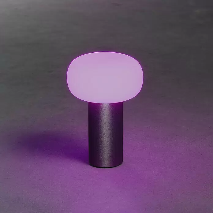 Konstsmide Akku-Tischleuchte Antibes - 2,5 W, L x B x H: 13 x 13 x 19 cm, Rost, Mehrfarbig - Eine moderne Tischlampe mit dunklem zylindrischem Sockel und einem leuchtenden ovalen Diffusor, der sanftes violettes Licht ausstrahlt.