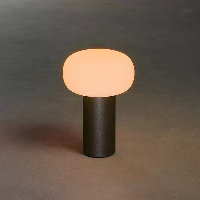 Konstsmide Akku-Tischleuchte Antibes - 2,5 W, L x B x H: 13 x 13 x 19 cm, Schwarz, Mehrfarbig - Eine leuchtende Tischlampe mit ovalem, transluzentem weißem Diffusor und dunklem zylindrischem Sockel.