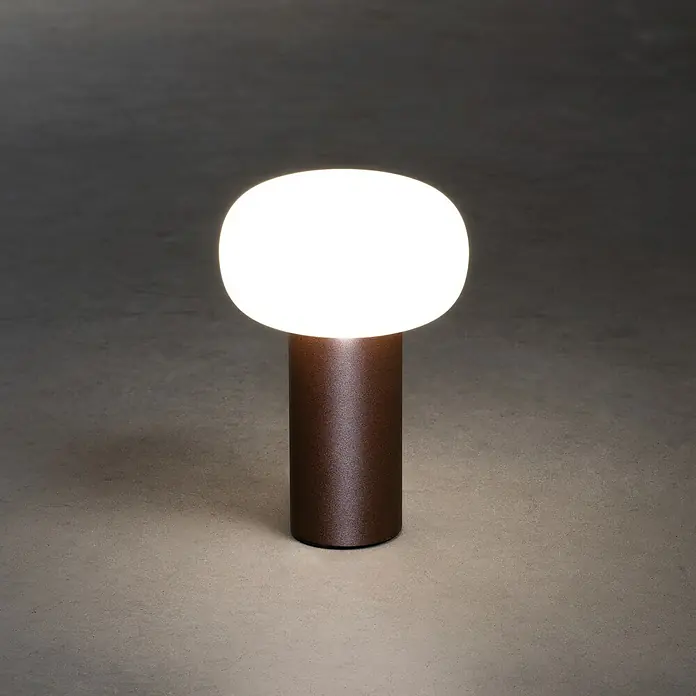 Konstsmide Akku-Tischleuchte Antibes - 2,5 W, L x B x H: 13 x 13 x 19 cm, Rost, Mehrfarbig - Nahaufnahme einer modernen Tischleuchte mit einem runden, leuchtenden Lampenschirm auf einem zylindrischen, bronzefarbenen Sockel.