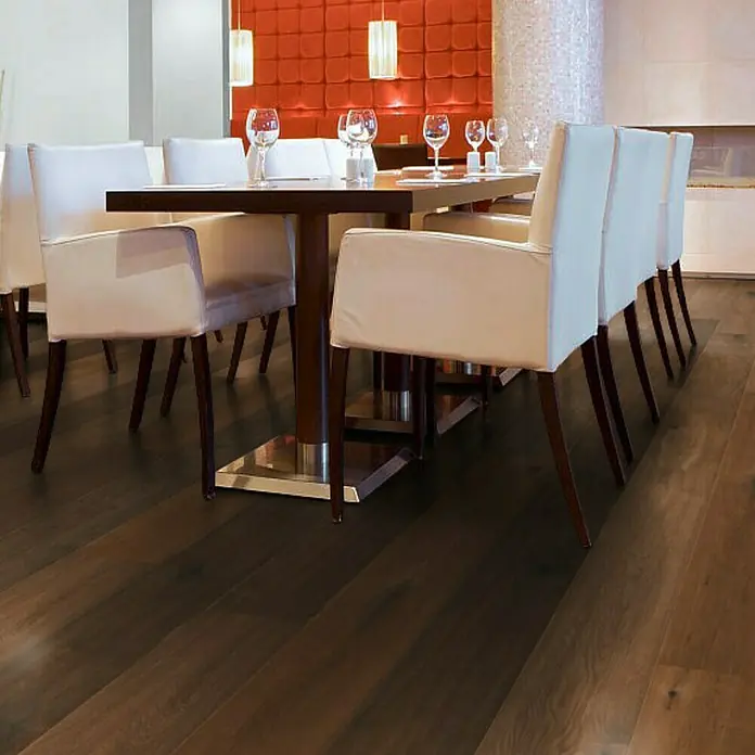 Parkettmuster Eiche Nero - 280 x 160 x 15 mm, Landhausdiele - Ein einladender Essbereich mit einem eleganten Holztisch und stilvollen weißen Stühlen auf einem dunklen Holzboden. Das warme Licht sorgt für Atmosphäre.