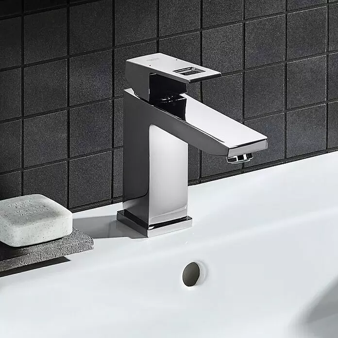 Grohe Eurocube Waschtischarmatur M-Size - Mit Zugstange, Chrom, Glänzend - Polierter Chrom-Wasserhahn auf einem weißen Waschbecken, vor dunklen Fliesen.