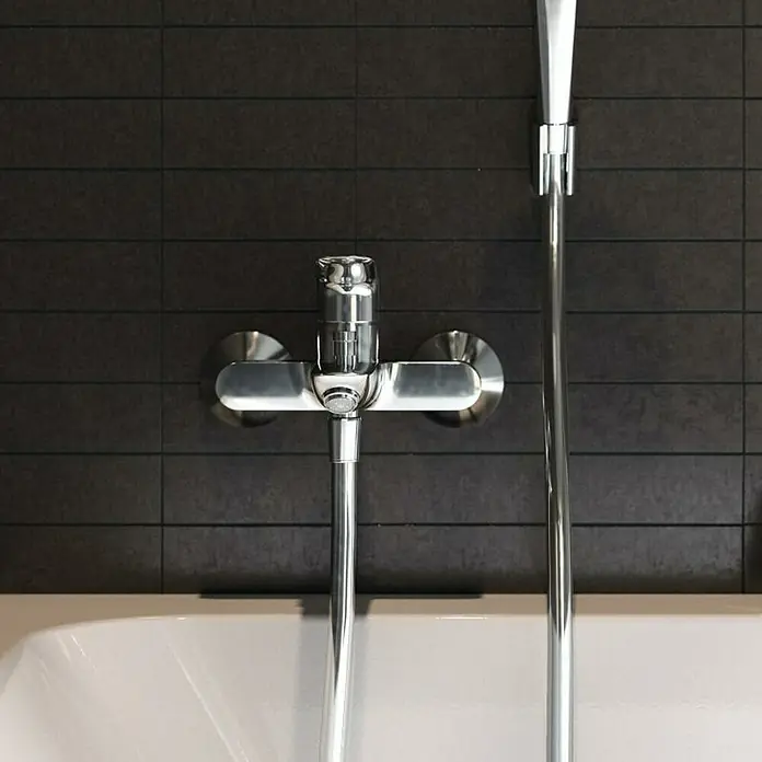 Hansgrohe Logis Badewannenarmatur Logis - Ausladung Armatur: 194 mm, Chrom, Glänzend - Nahaufnahme eines eleganten, verchromten Badewannenmischers mit Handbrause vor einem dunklen, modern gefliesten Hintergrund.